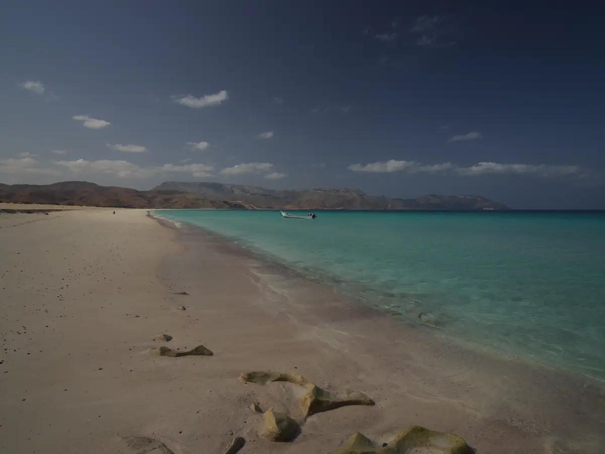 An empty white beach at Shuab, with a boat moored offshore and turquoise shallows
